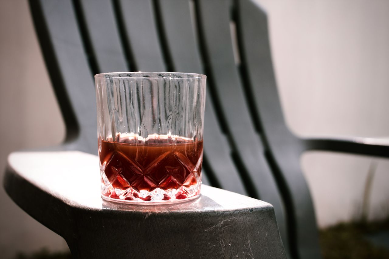 A close-up of a cocktail in a glass on a chair armrest, outdoors with natural light.