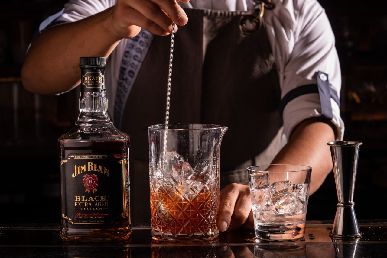 who-we-are-img Bartender preparing a whiskey cocktail with Jim Beam in a stylish bar setting.