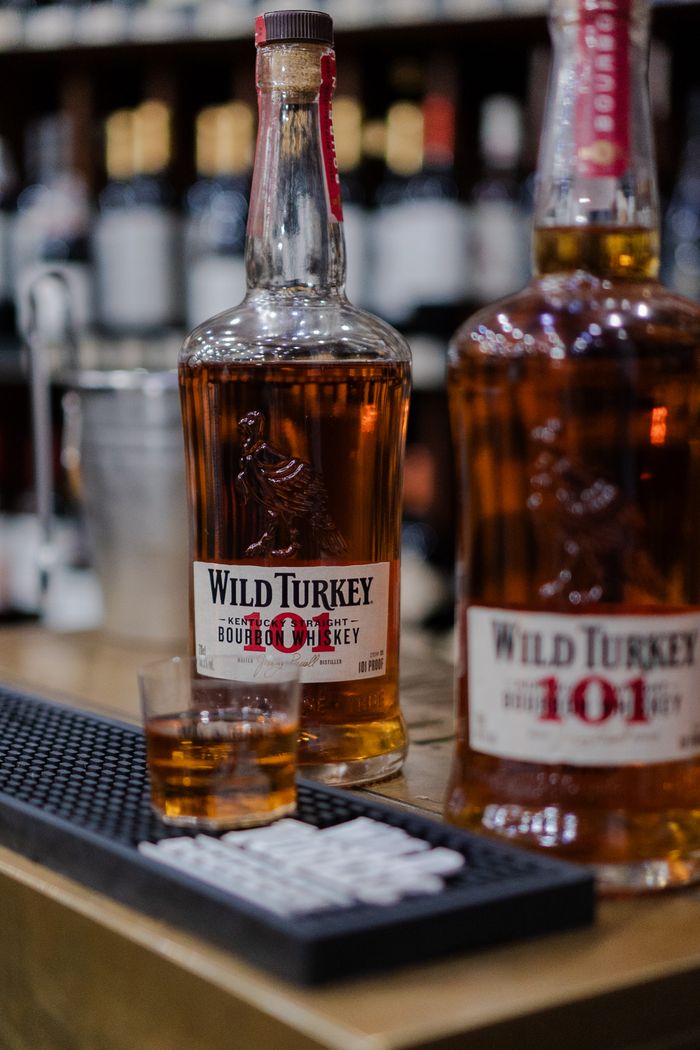 Close-up of Wild Turkey bourbon whiskey bottles and a glass on a bar counter.