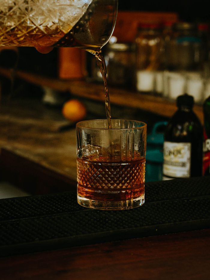 A close-up shot of whiskey being poured into a textured glass, capturing the golden hues and ambiance of a bar.